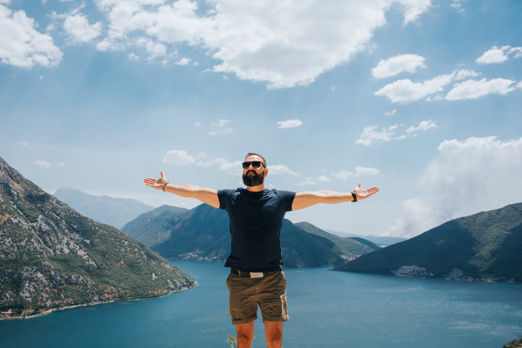 Man arms wide open in front of lake and mountains