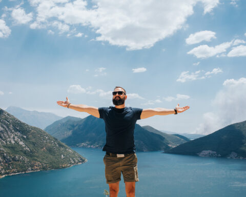 Man arms wide open in front of lake and mountains